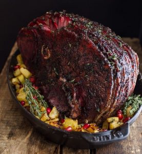 Chipotle Pineapple Jerk Glazed Ham sitting in a roasting pan on top of vegetables and chopped pineapple.