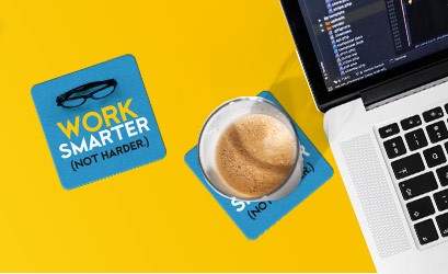 Laptop, personalized drink coasters, and a beverage on top of one of the coasters. the other coaster reads "Work Smarter Not Harder," and includes a graphic of a pair of reading glasses.