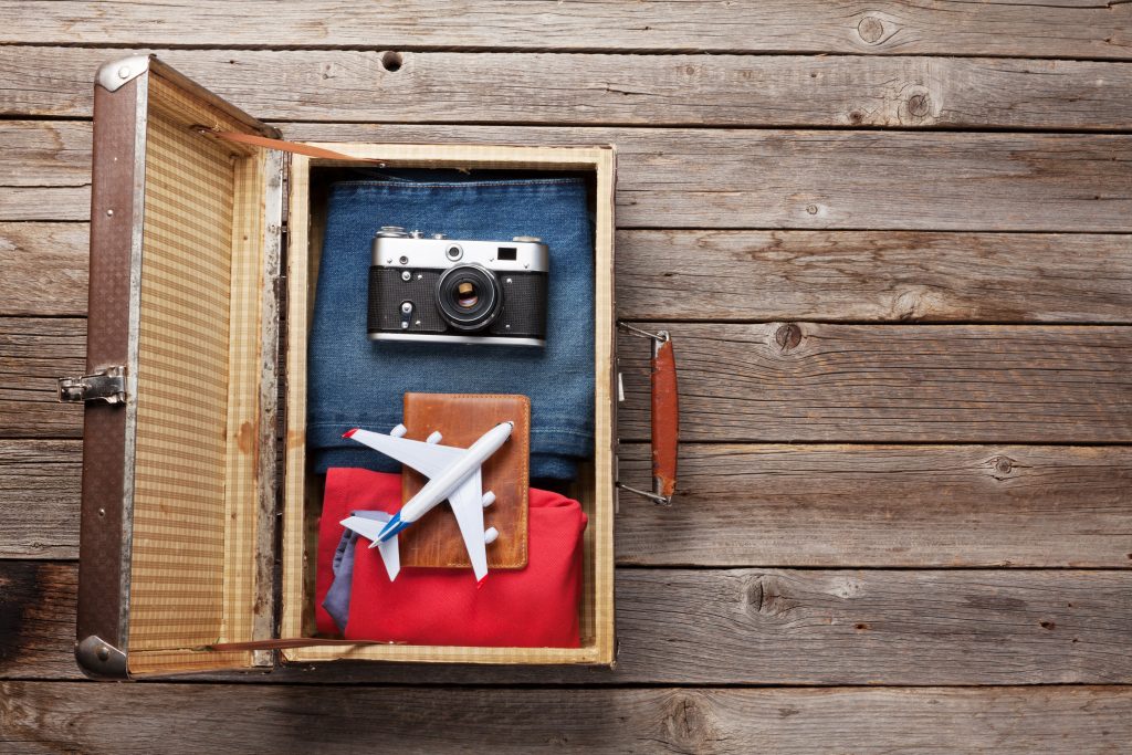 Suitcase with clothes and travel accessories. Tourist and vacation things on wooden background with space for your text. Top view flat lay