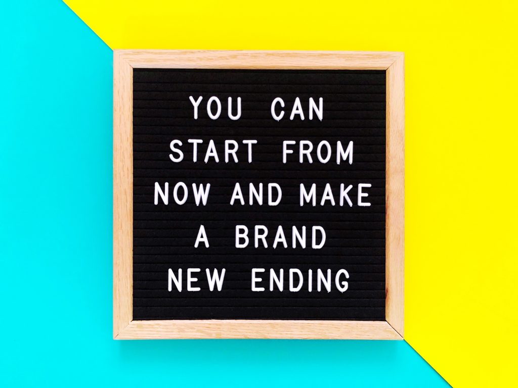 Light blue and yellow background with a tan and black sign that reads, "YOU CAN START FROM NOW AND MAKE A BRAND NEW ENDING" in all caps.