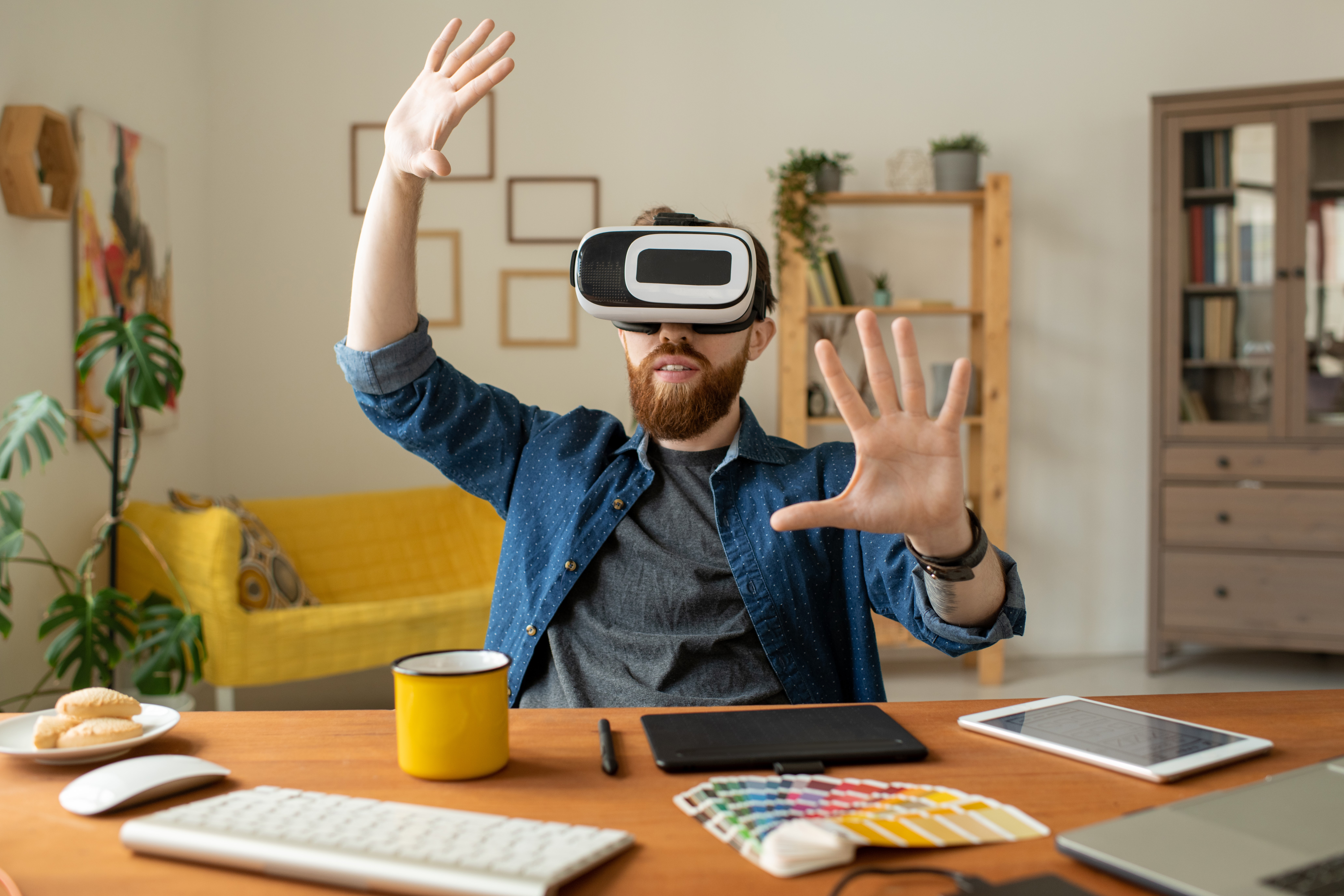 Content curious bearded man sitting at desk in home office and gesturing hands while testing new app in virtual reality goggles