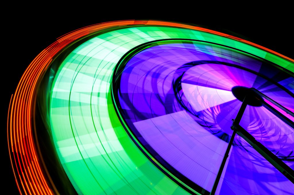 Spinning neon Ferris Wheel ride at amusement park at night