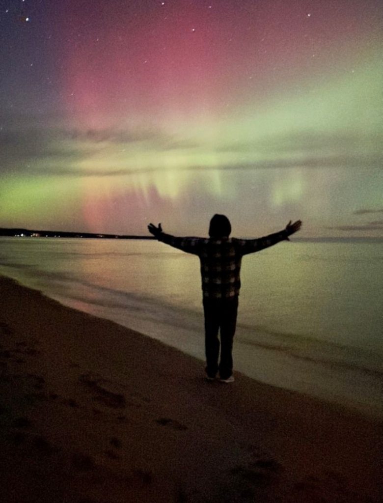 Silhouette of a man on a beach underneath the Northern Lights.